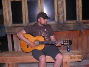 Sean plays an acoustic guitar on a wood bench.