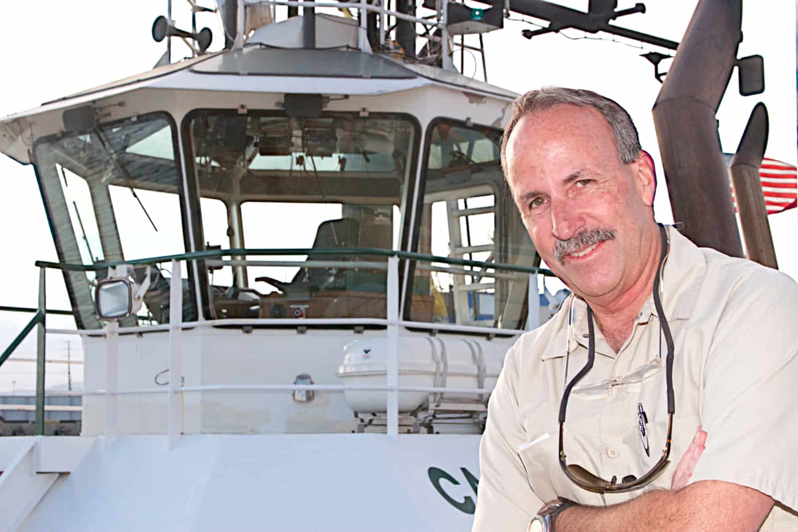 Guy crosses his arms and smiles in front of a Foss tugboat.