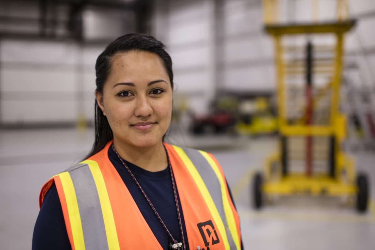 Roselyn poses in a warehouse wearing an orange NAMS reflective vest.