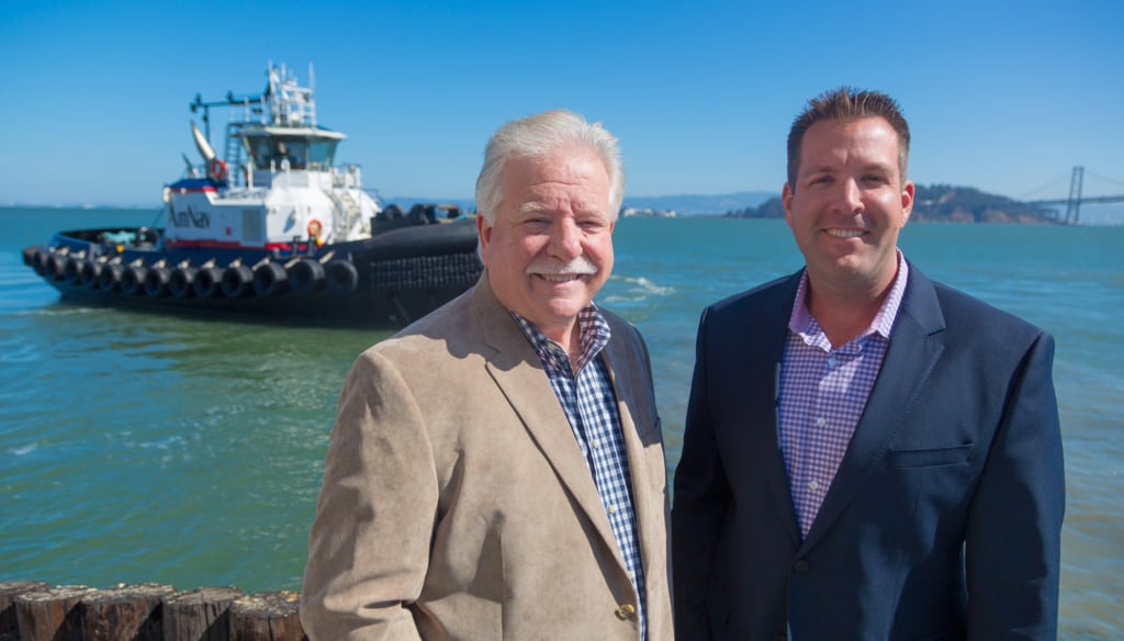 Dave and Milt Merrit smile in front of an AmNav tractor tugboat coming into dock in the San Francisco bay.