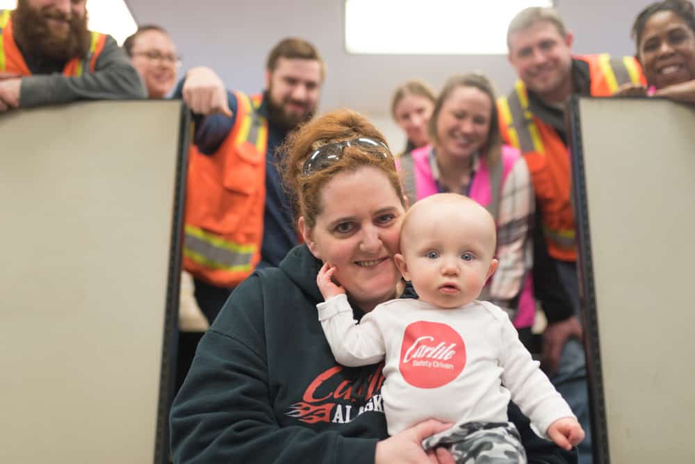 Sprinkle holds her baby grandson, who rests his hand on her face, as Carlile employees gather around them for a photo.