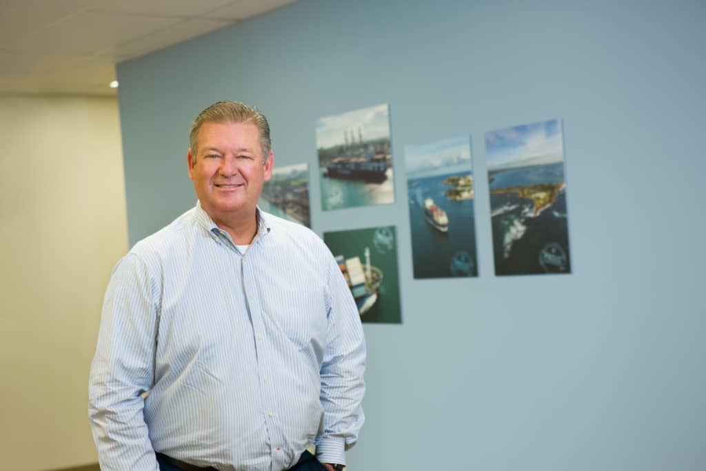 Bob smiles in an office building, standing in front of maritime images.