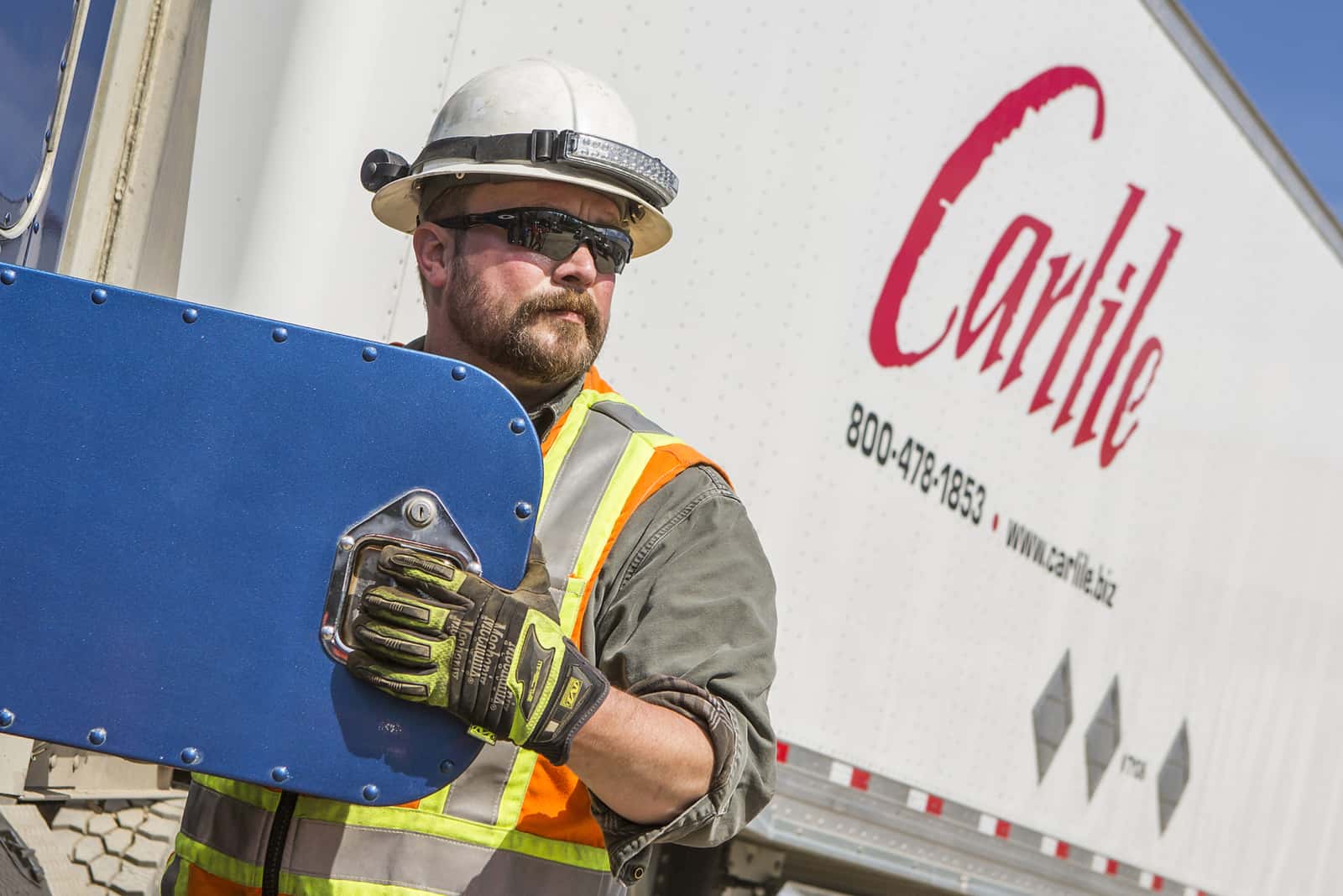 Eyth wearing a hardhat, sunglasses, safety vest, and thick gloves opens a compartment on his Carlile rig.