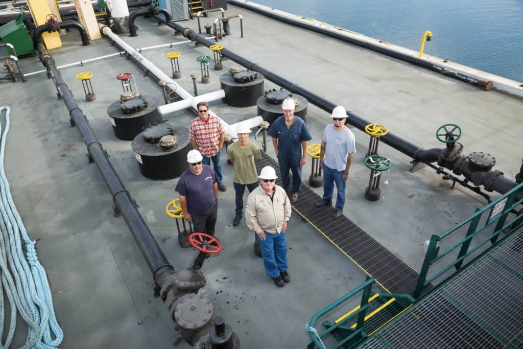 Ron stands with his team aboard a barge, all wearing hard hats.