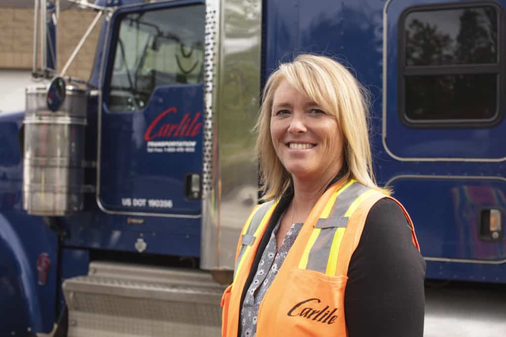 Christen poses in front of a Carlile truck wearing a Carlile orange vest.