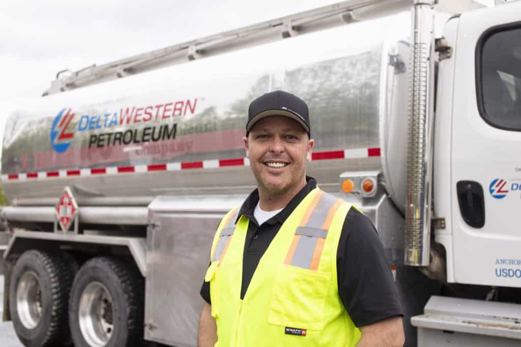 Leon poses in front of a Delta Western Petroleum truck wearing a yellow reflective vest.