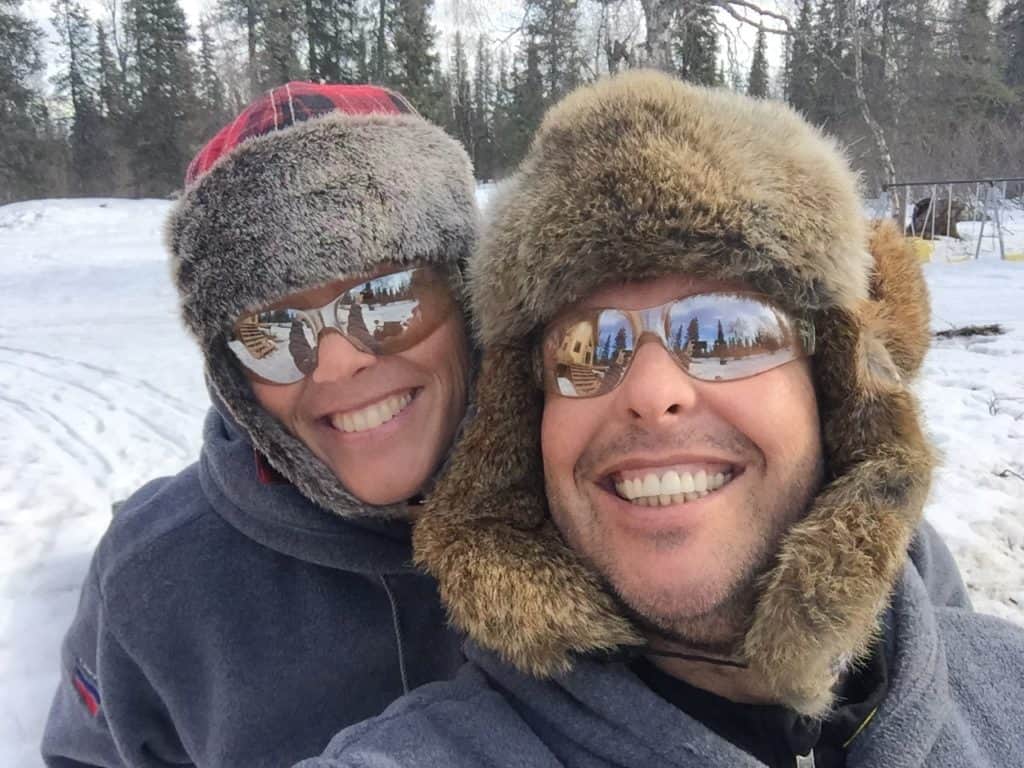 Christen and Leon wearing furry hats and fleece jackets in a snowy forest.