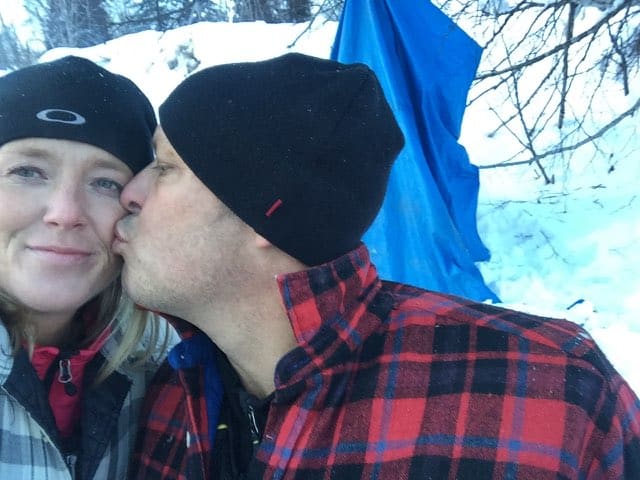 Leon kisses Christen on the cheek in a snowy forest.