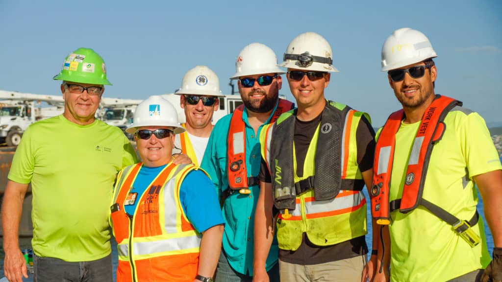 Wagoner (left) with partners pose for the camera, all wear hard hats and reflective gear.