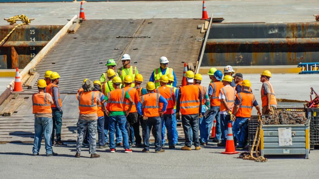 A team gathers in reflective vests and hard hats in front of a barge gangway.