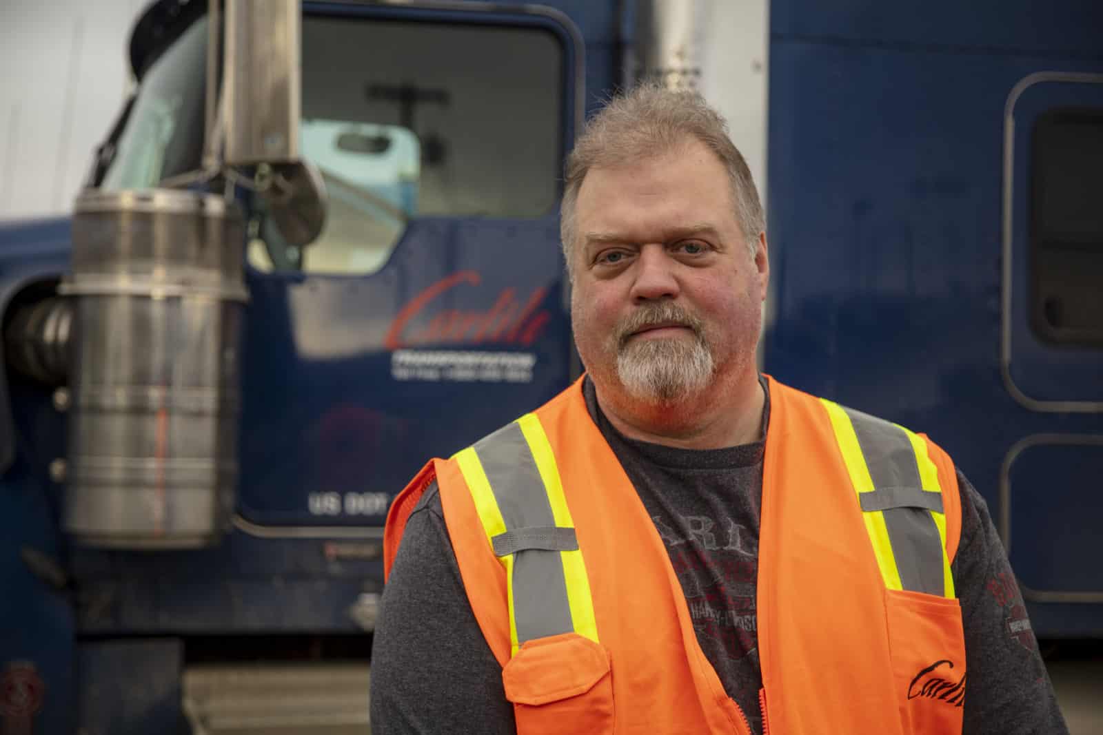 Tony poses in an orange reflective vest in front of a Carlile truck.