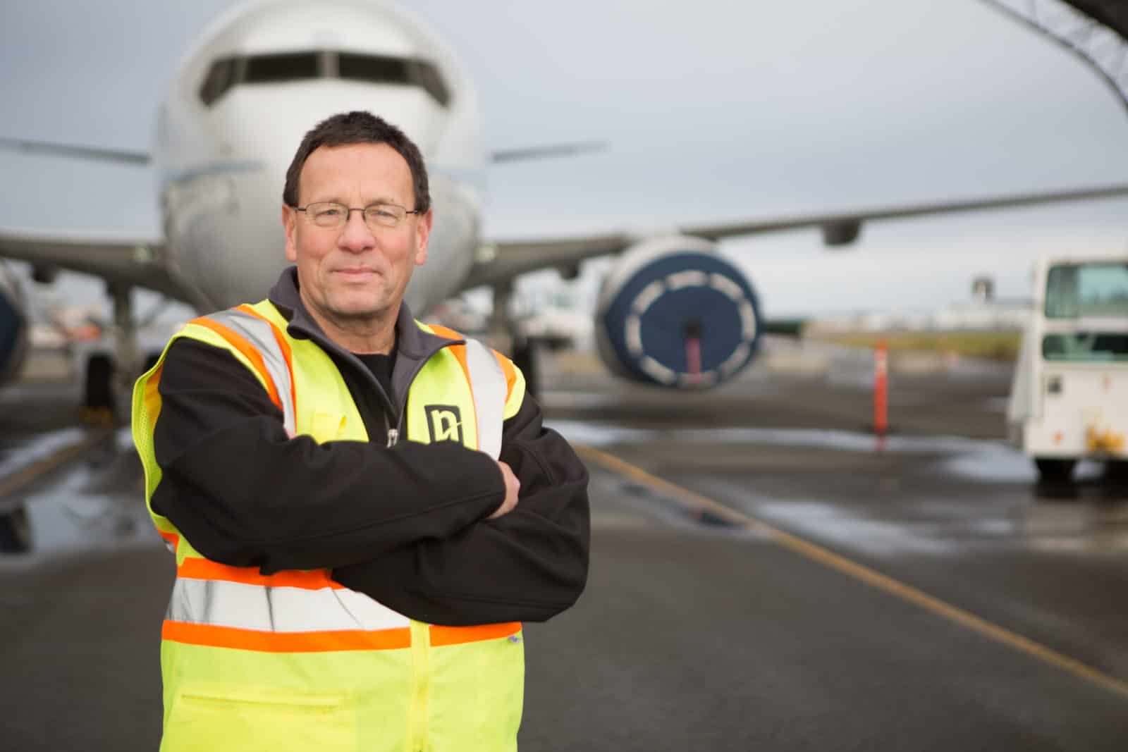 Parry crosses his arms in front of an airplane in a reflective yellow vest.