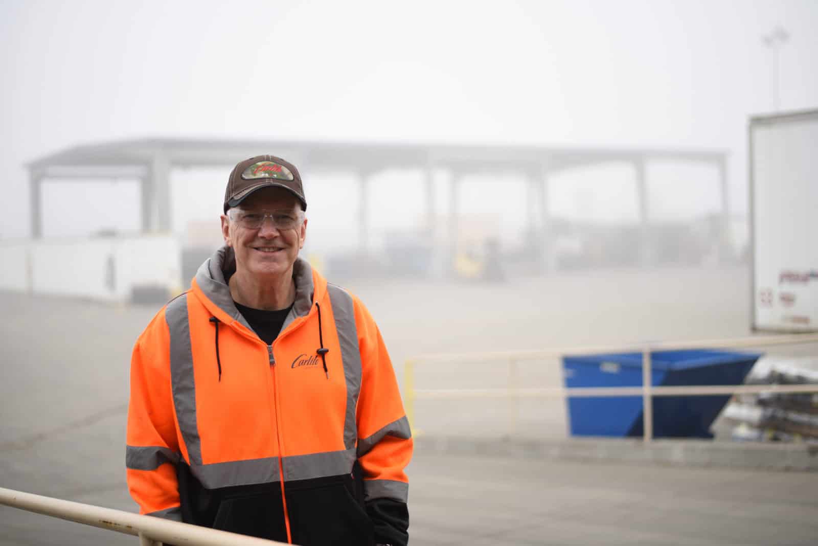 Clay stands in a foggy industrial yard in an orange Carlile hoodie.