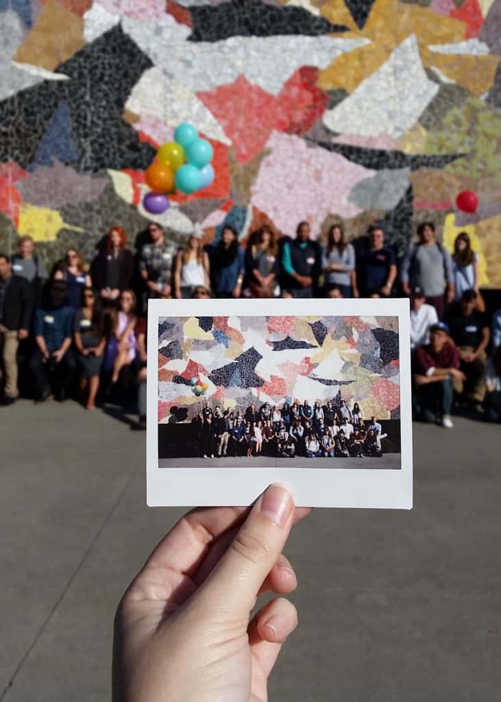 An image of a polaroid, showing a group of people posing before a Horiuchi mural at the Seattle Science Center, behind the polaroid is the same group posing in front of the same mural.