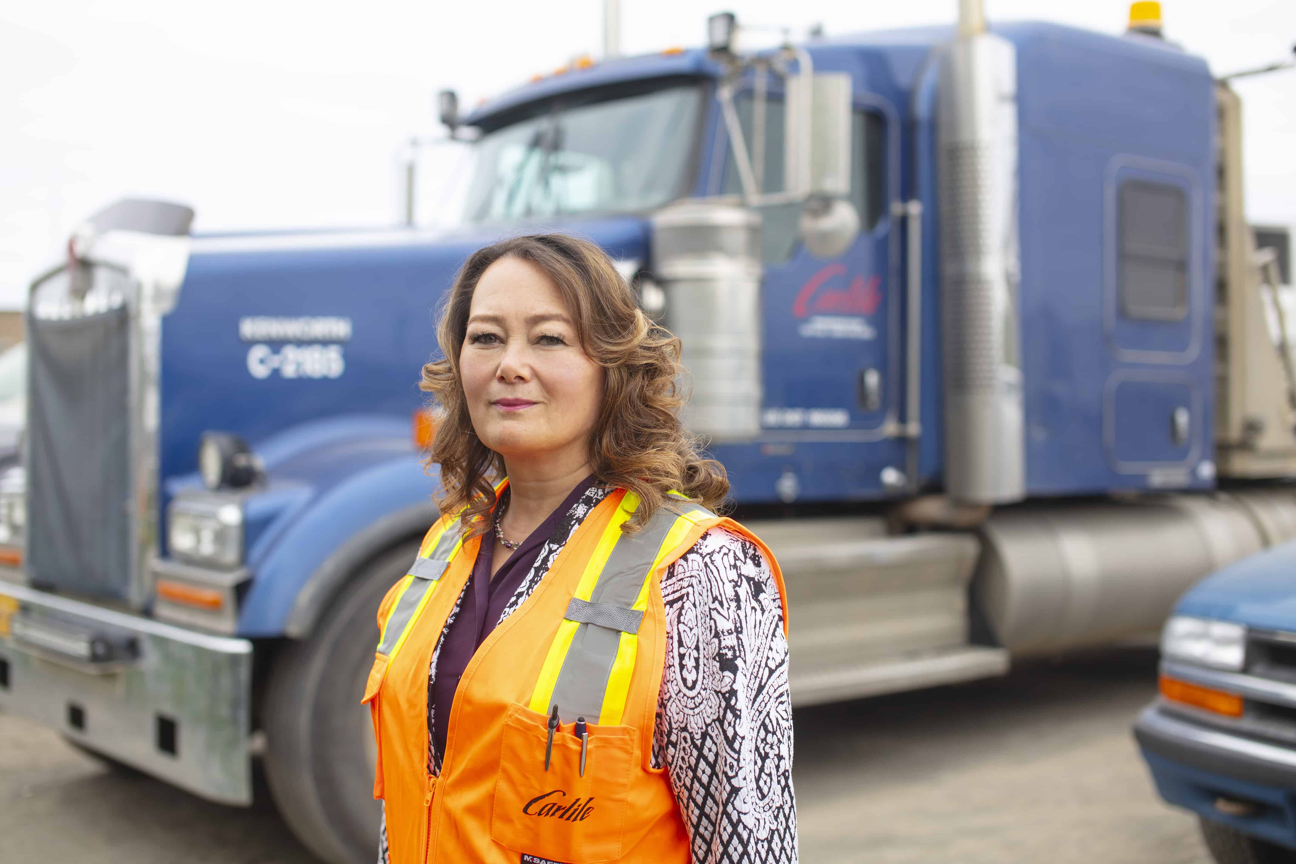 Lisa wears an orange Carlile reflective vest in front of a Carlile truck cab.