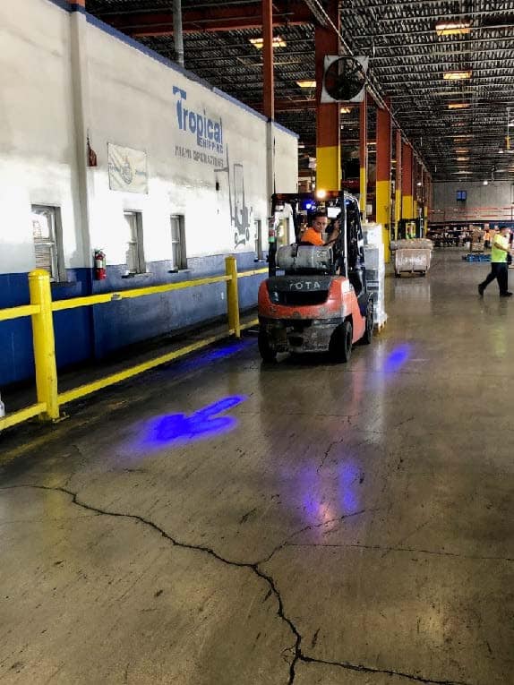 In a Tropical warehouse a bright blue LED paints an arrow and box around a forklift.