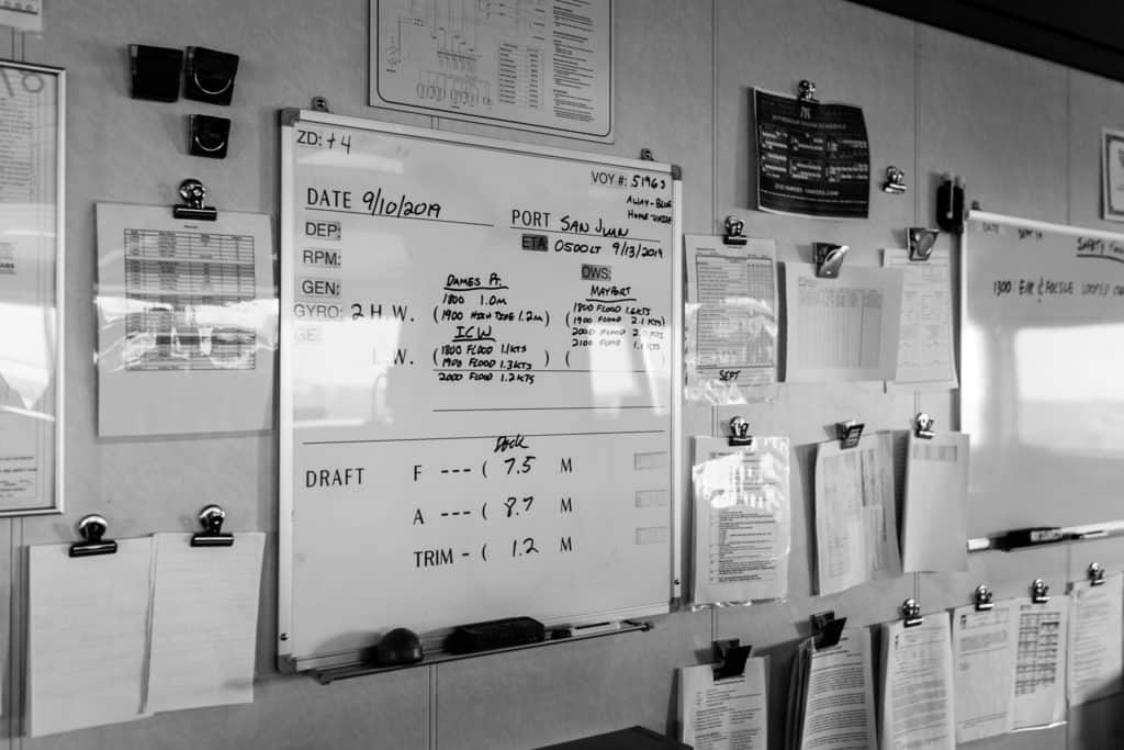 Black and white photo of a wall filled with charts whiteboards and detailed information.