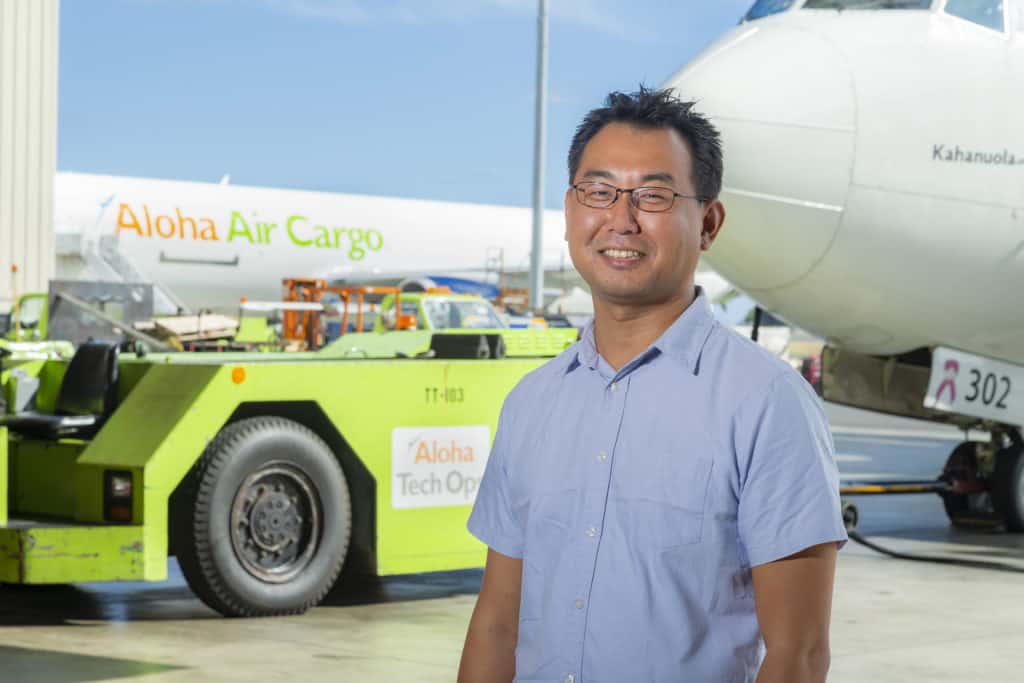 Ko smiles on Aloha Air Cargo tarmac. Two cargo planes sit behind him.