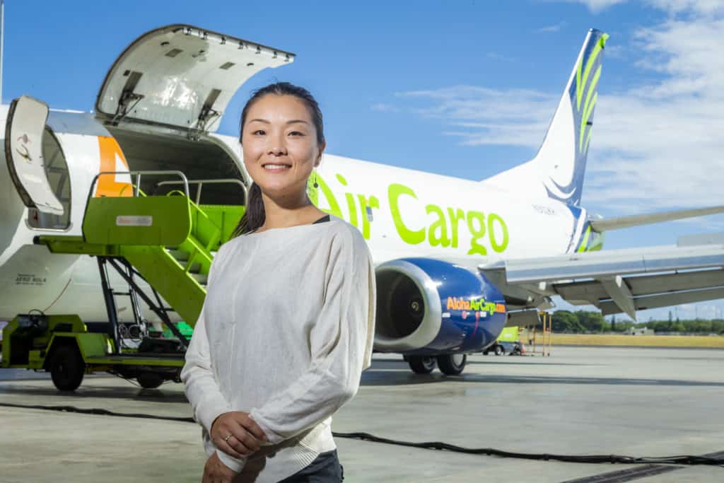 Lan smiles in front of an Aloha Air Cargo plane with doors open.