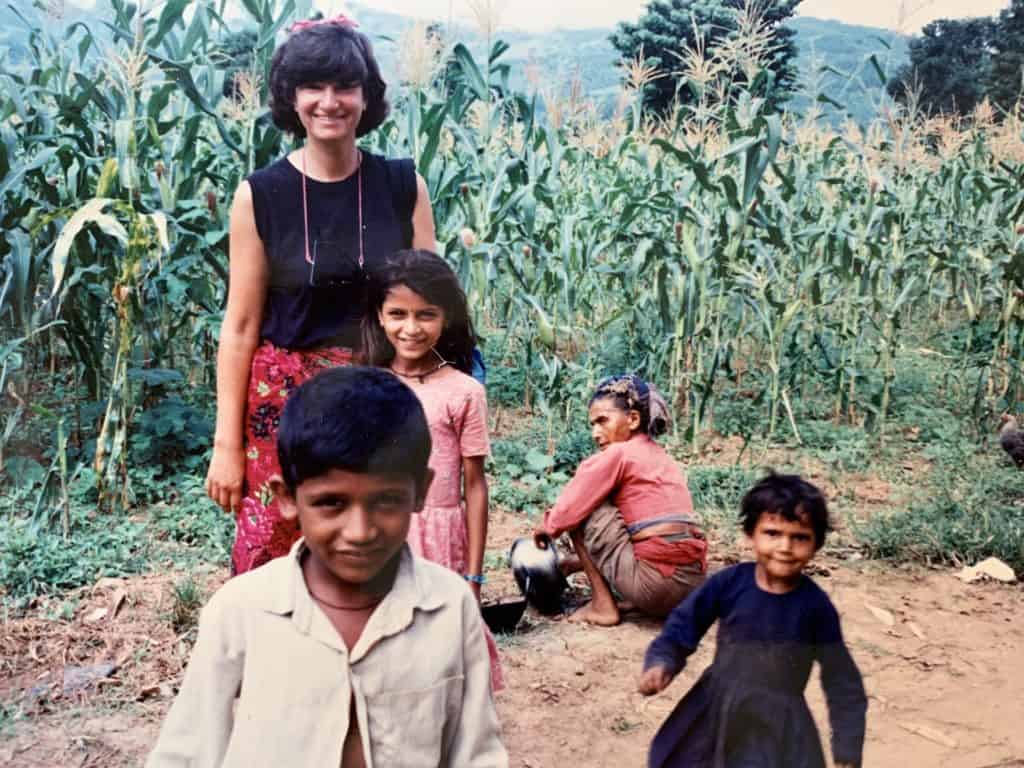 A young Erin smiles with some children in a corn field in Nepal.