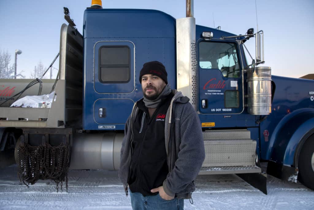 Jeremy poses in a fleece, hoodie, and beanie, in front of a Carlile truck.