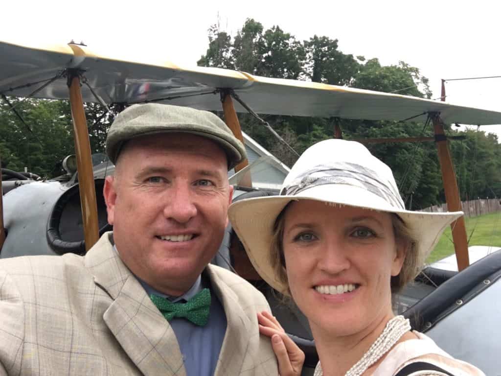 Adam poses with his wife in front of an old biplane.