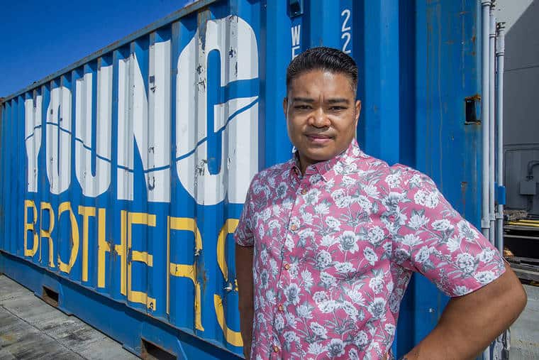Jay poses in a colorful button up short sleeved shirt in front of a YB shipping container.