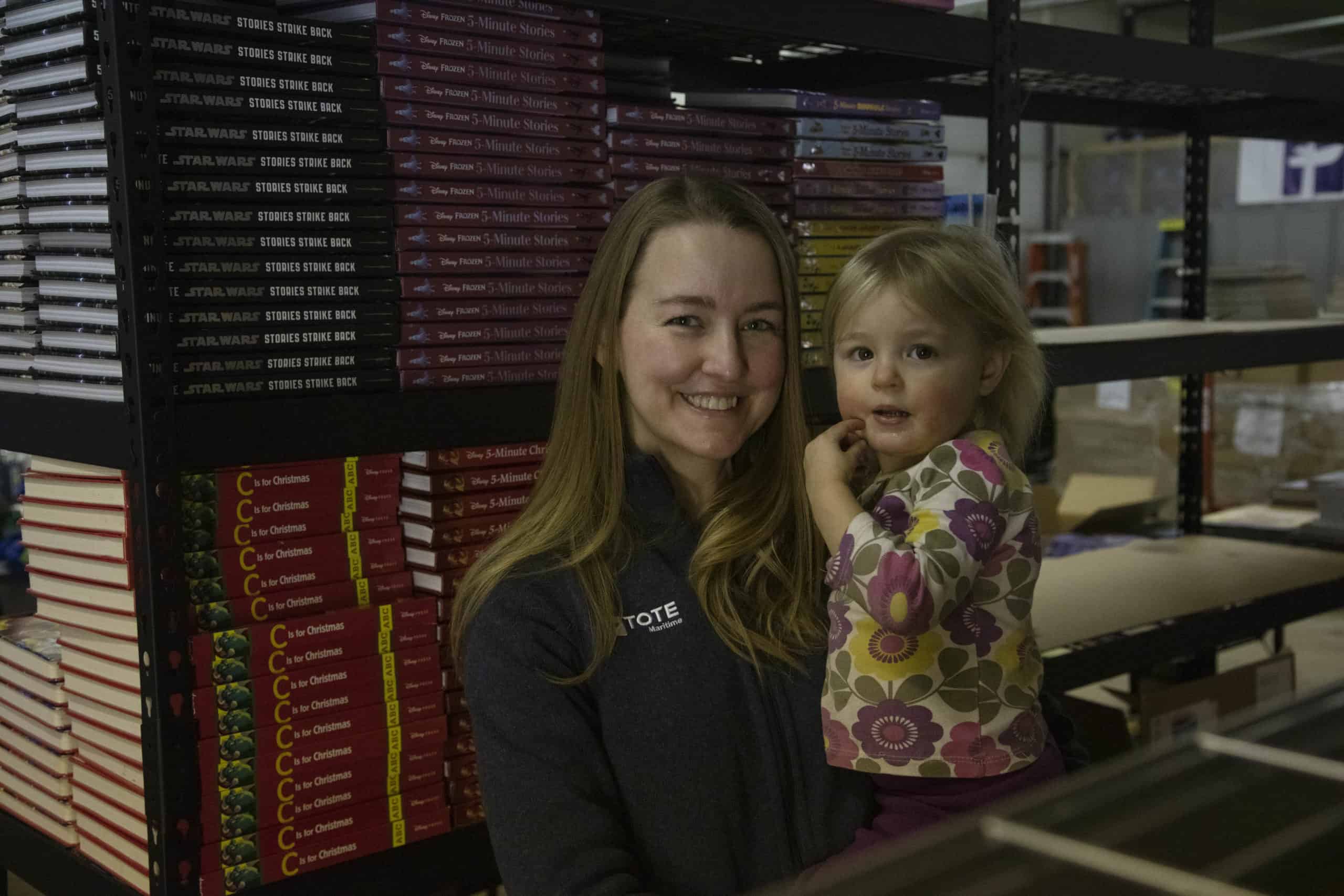 Milena holds her daughter in front of shelves of stacked books.