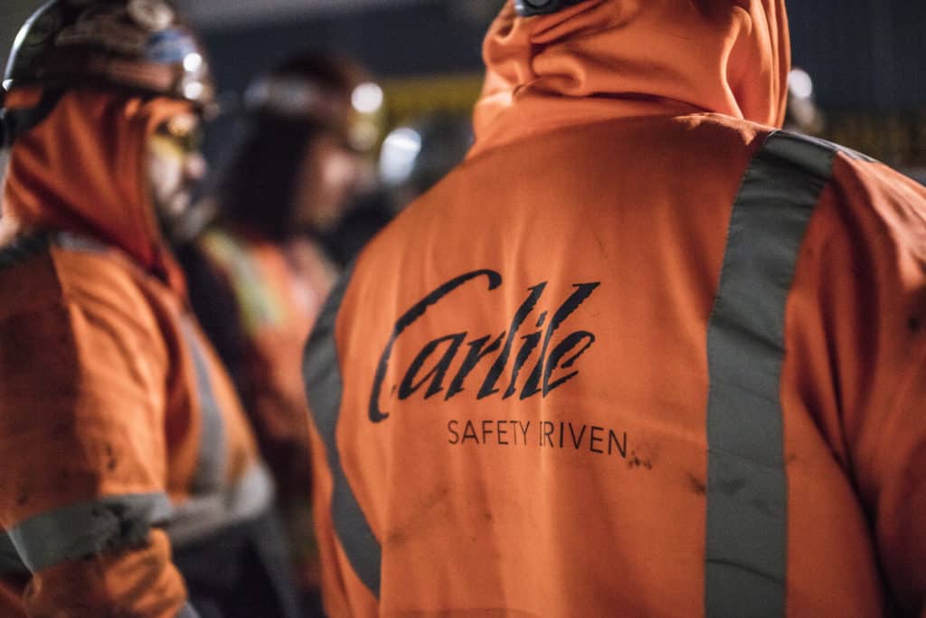 Close up of the back of an orange reflective hoodie reads, "Carlile, Safety Driven."