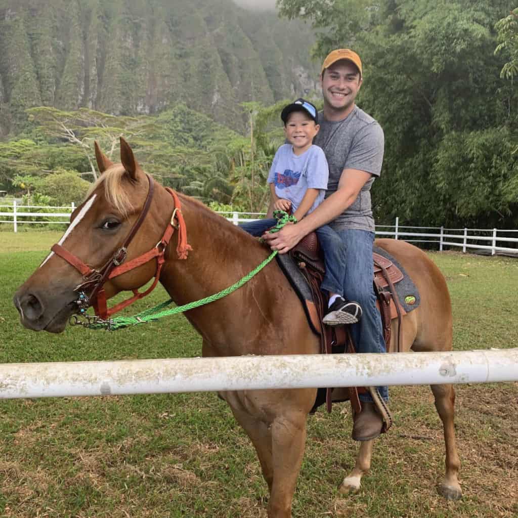 Case rides a horse with his son in his lap. Mountains tower behind them.
