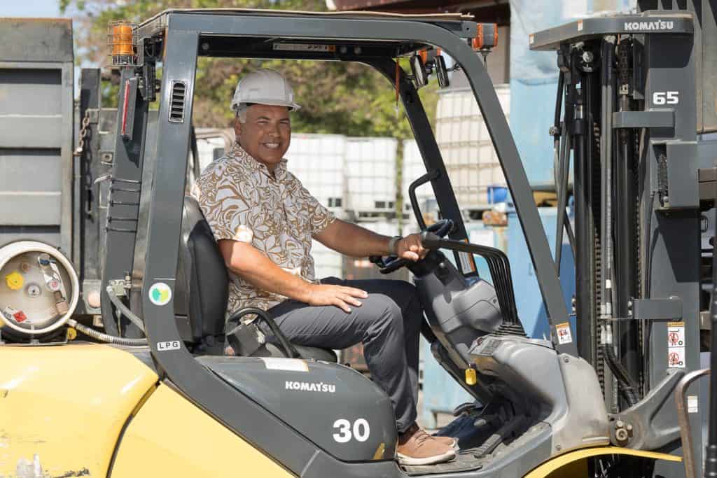 Kimo Haynes rides a forklift wearing a hardhat.