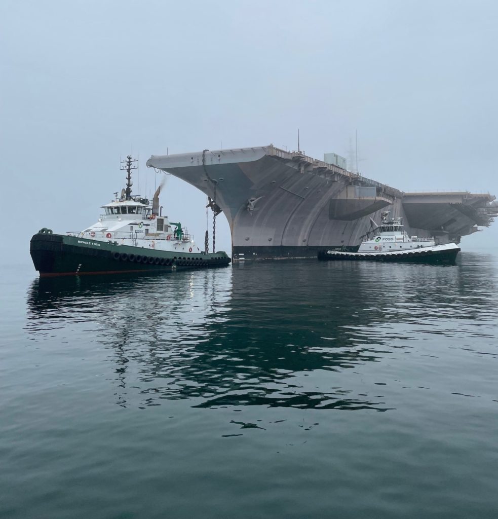 Surrounded by fog, two Foss tugs pull the USS Kitty Hawk through calm waters.