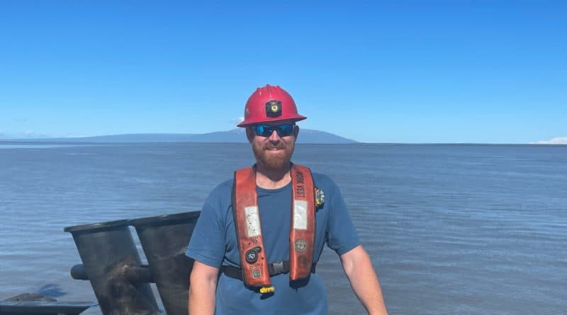 Eric Nyce smiles in hard hat and PFD. A vast stretch of ocean behind him.