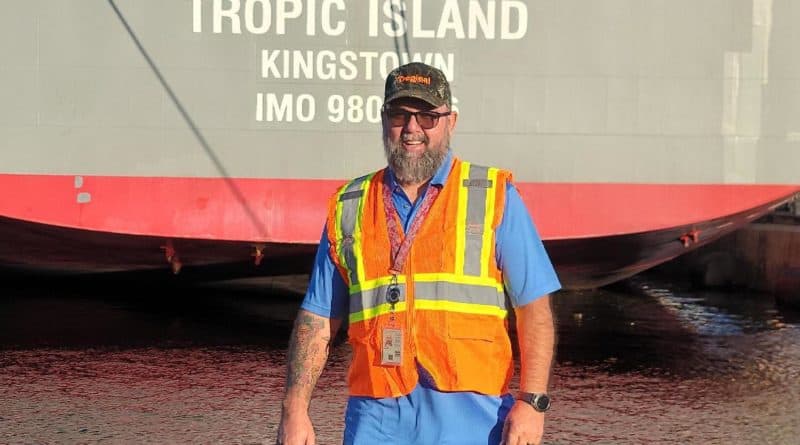 Robert Ackley stands before the stern of the Tropical ship Tropic Island.