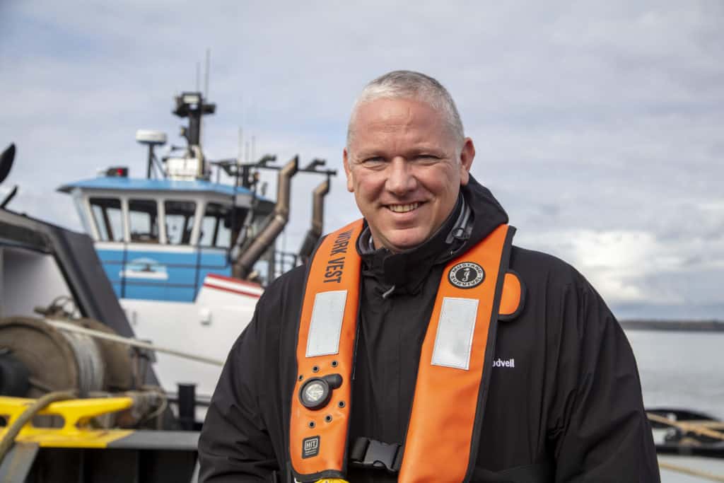 Johnson, wearing orange PFD, smiles in front of a CITB tug.