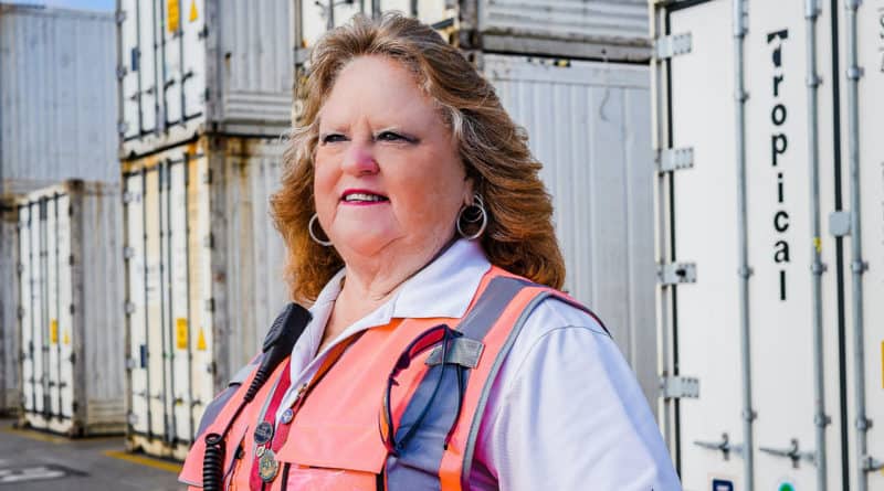 Merrilee Gorman smiles and looks off into the distance in an orange reflective vest in a Tropical container yard.