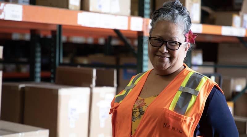 Vicky Tecson smiles in an orange reflective vest in a warehouse.