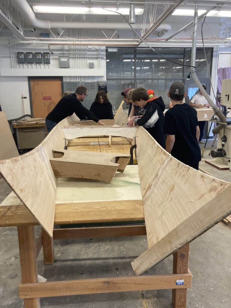 Students work on the structure of a boat in a workshop.